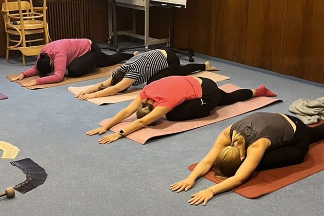 Mehrere Mitarbeitende eines Unternehmens machen gemeinsame Yoga-Übungen in einer Trainingshalle.